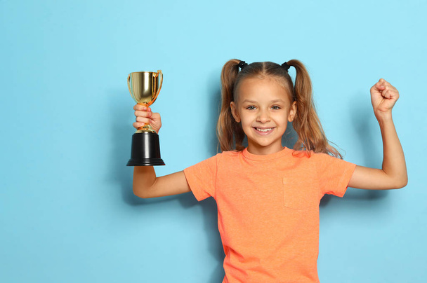 Happy girl with golden winning cup on blue background - Fotografie, Obrázek