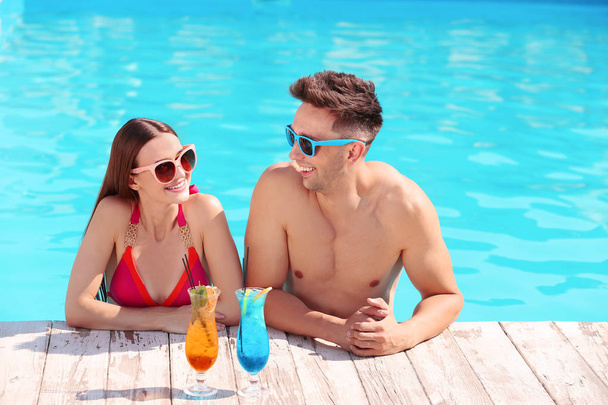 Happy young couple with cocktails in swimming pool - Foto, Imagem