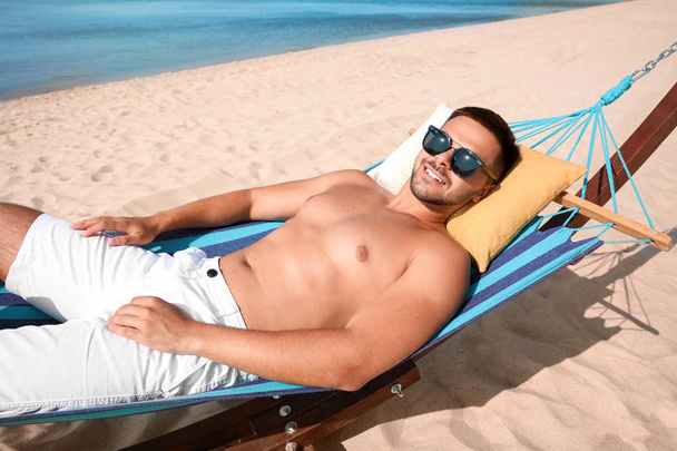 Young man relaxing in hammock on beach - 写真・画像
