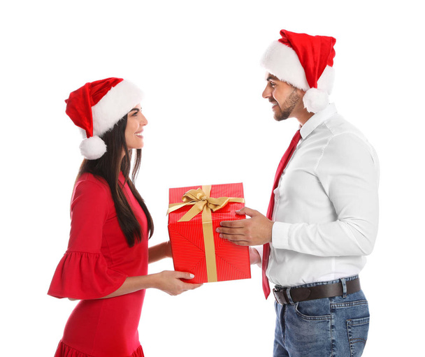 Lovely young couple in Santa hats with gift box on white background. Christmas celebration - Φωτογραφία, εικόνα