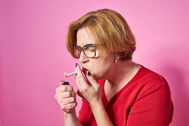 Smoker Portrait of an old woman smoking a cigarette. Isolate on a red background. - Foto, Imagen