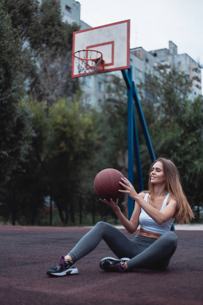 Meisje op een basketbalveld met een bal. Sportkleding gekleed in leggings en top. - Foto, afbeelding