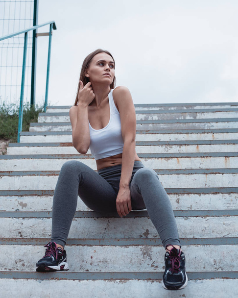 A beautiful girl is sitting on the steps. Sportswear in leggings and sneakers. - Fotoğraf, Görsel