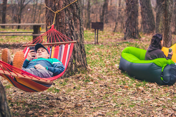 молодые люди отдыхают на природе. мужчина лежит в гамаке женщина сидит на надувном матрасе
 - Фото, изображение