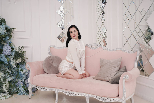 Preciosa mujer morena en pijama blanco lindo resto con sofá rosa solo en apartamento blanco solo
 - Foto, imagen