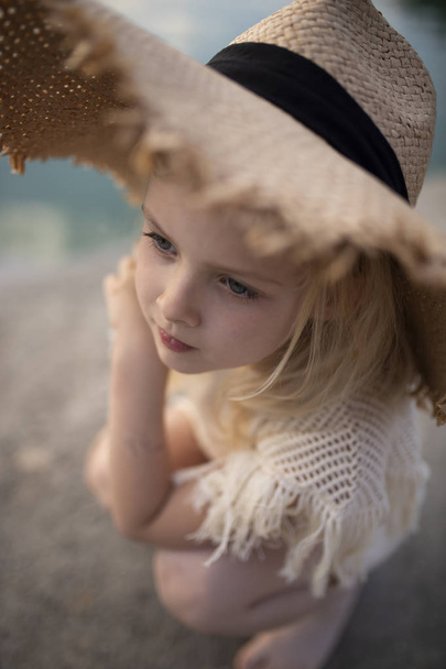 kleines nettes Mädchen in stilvoller Kleidung auf einem Hintergrund aus Felsen. Sommerporträt eines kleinen Mädchens mit Hut und Baumwollkleidung für eine Zeitschrift oder Werbung - Foto, Bild