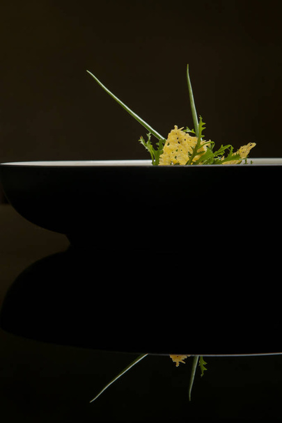 絶妙なミニマルなスタイルの料理は、反射と黒のボウルで提供されます。クリエイティブなレストランの食事コンセプト。オートクチュール食品。ファインダイニングコンセプト. - 写真・画像