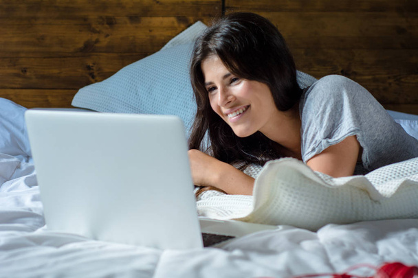 Young woman using her laptop on bed - Fotó, kép