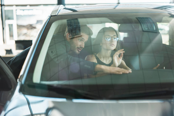 handsome man manager consulting young woman client while choosing new car in dealership - Foto, immagini