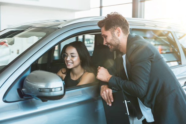 handsome man manager consulting young beautiful woman client while looking for new car in dealership center - Photo, Image