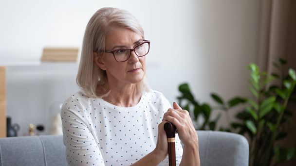 Upset mature woman holding wooden cane, thinking about future - Foto, Imagen
