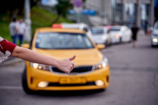 Image from back of woman with outstretched hand stopping taxi in afternoon on blurred background. - Fotó, kép