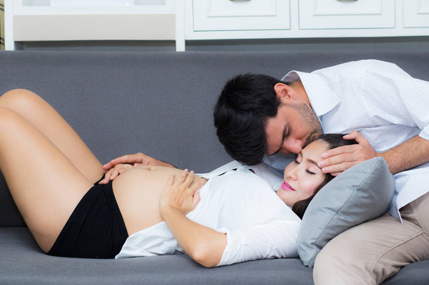 夫は妊娠中の腹で妻の額にキスをしながら - 写真・画像