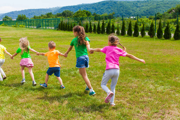 Children play holding hands on the green grass, back view - Photo, Image