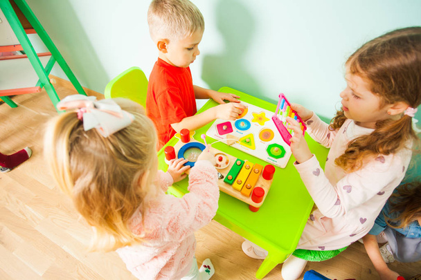 Toddler boy and girls sitting at the table in playroom. - Valokuva, kuva