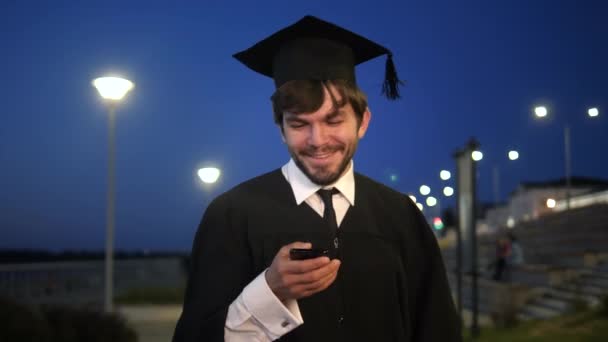 Estudiante graduado caminando por la noche y mensaje de texto en el teléfono
. - Imágenes, Vídeo