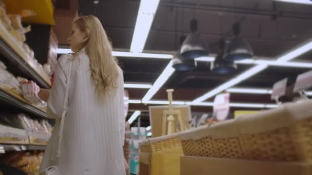 Attractive girl customer is buying bread in bakery department is shop, smelling it, smiling and putting in shopping trolley. Healthy lifestyle and supermarket concept - Filmagem, Vídeo