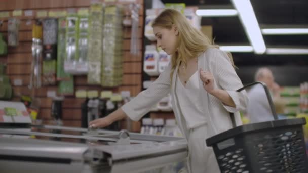 Dívka v supermarketu vydělá z chladničky zmrazené potraviny, které čtou složení výrobku a vloží jej do košíku. - Záběry, video