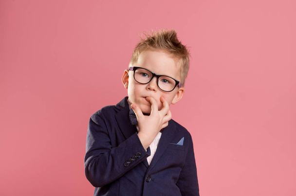 School boy nervously biting nails. Bulling and childhood psychology concept, Child boy in uniform, glasses and backpack isolated on pink. Kid portrait with finger in mouth - Photo, image
