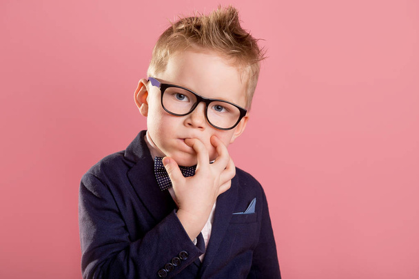 School boy nervously biting nails. Bulling and childhood psychology concept, Child boy in uniform, glasses and backpack isolated on pink. Kid portrait with finger in mouth - Photo, image