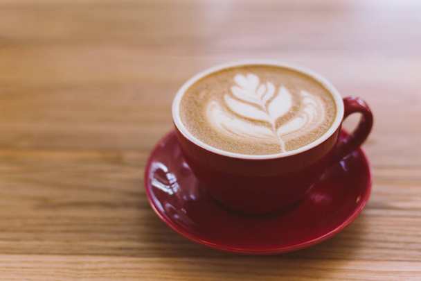 Šálek cappuccina s Latte art na dřevěném podkladu. Červený keramický pohár. - Fotografie, Obrázek