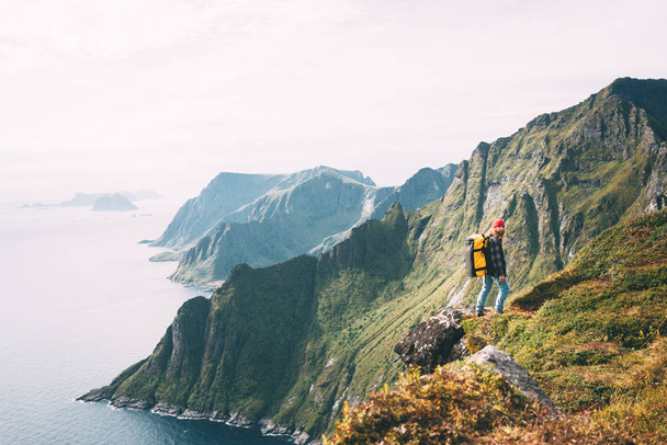 Alone man expeditor wearing professional backpack standing on the edge cliff mountain above sea and looking on epic high landscape. Lifestyle adventure vacation - 写真・画像