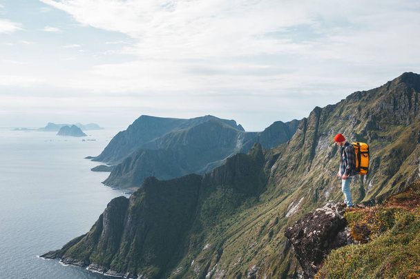 Man wearing professional backpack traveling alone on the high mountains. Traveler standing on the edge cliff rock above sea and enjoying epic view - 写真・画像
