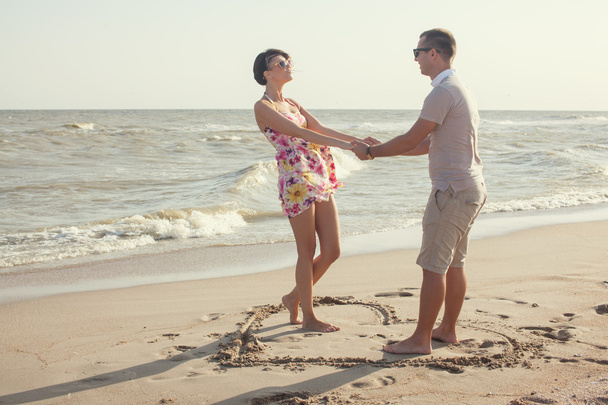 A heart shape drawn in the sand. Couple standing inside heart picture on the sand. Summertime fun - Photo, Image