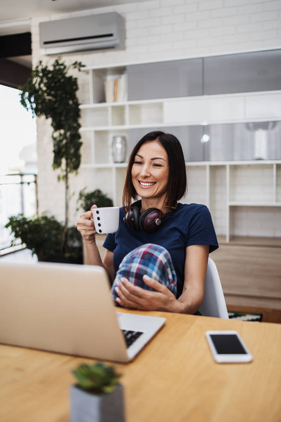 Attractive and happy middle age female freelancer is working and smiling at her home. Modern living room in background. Freelancing job concept. - Zdjęcie, obraz