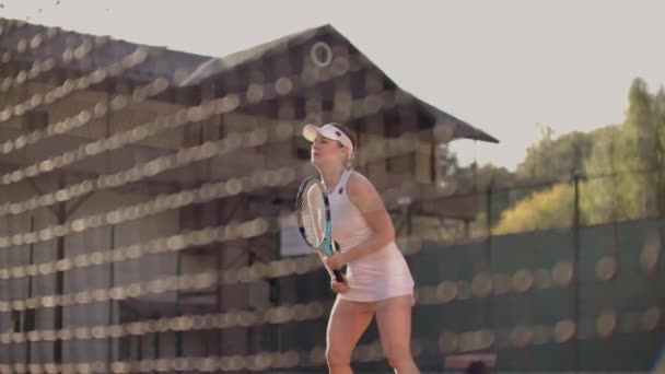 Uma mulher profissional em um terno apertado branco bate a bola com uma raquete e joga dinamicamente na quadra de tênis
 - Filmagem, Vídeo