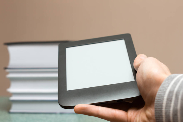 Modern e-book in de hand tegen de achtergrond van een stapel dikke papieren boeken. Hand met een e-book. Close-up met selectieve focus. Opleidings-en technologie concept - Foto, afbeelding