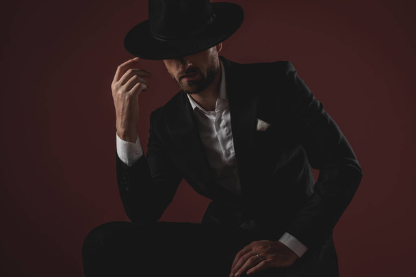 mysterieuze jonge man dragen Tuxedo en arrangeren hoed - Foto, afbeelding