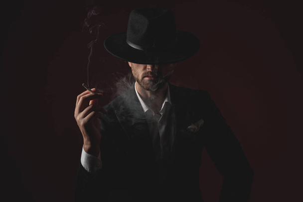 enigmatic young man smoking on black background - Photo, Image