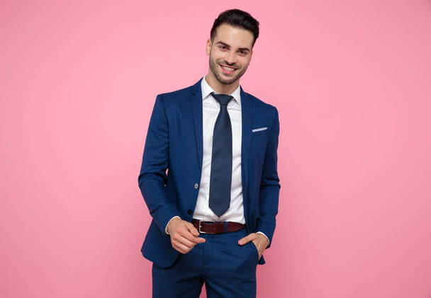 attractive young man wearing navy blue suit on pink bakground - Фото, изображение