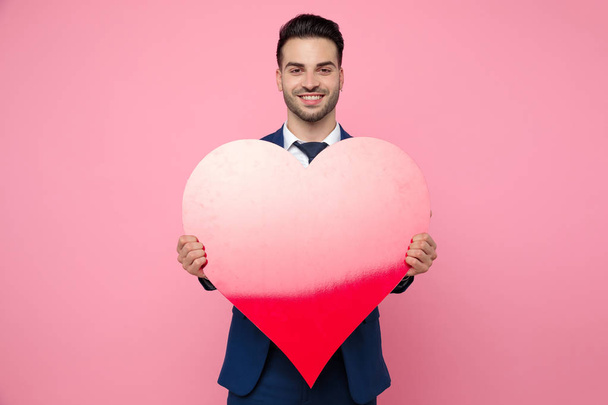 pohledný muž, který drží srdce na růžovém pozadí ve studiu - Fotografie, Obrázek