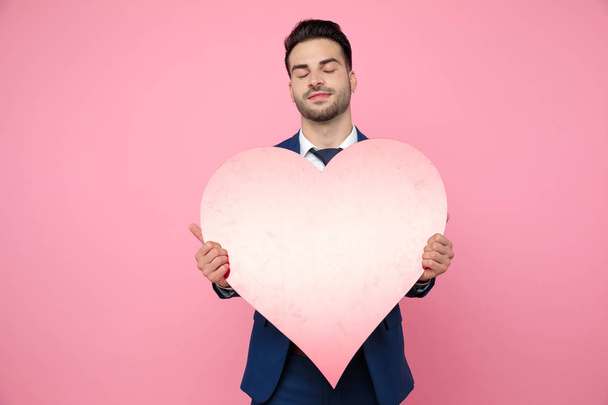 attractive young man holding heart on pink background - Fotó, kép