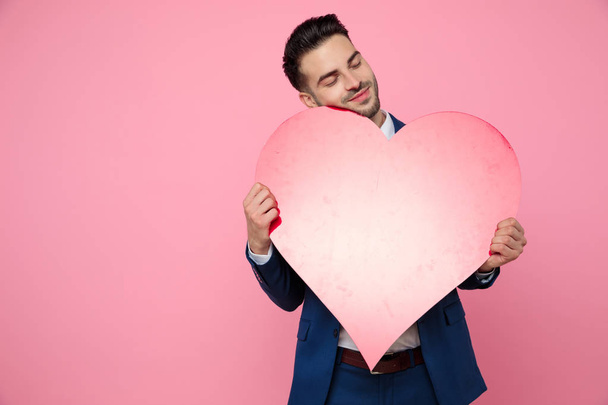 jovem atraente segurando um coração no fundo rosa
 - Foto, Imagem