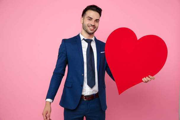 attractive young man holding a heart on pink background - Photo, Image