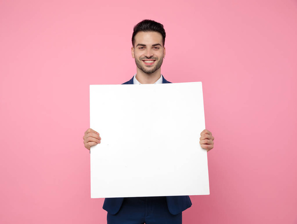 attractive young man holding empty board on pink background - Fotó, kép