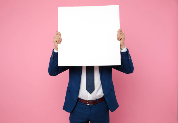 attractive young man holding an empty board on pink background - Foto, immagini