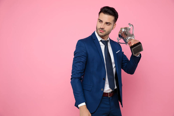 pohledný mladý muž, který drží pohár vítězného na růžovém pozadí - Fotografie, Obrázek