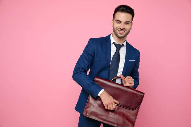 attractive young man holding suitcase on pink background - Foto, afbeelding