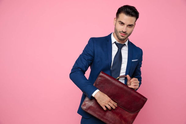 handsome young man holding suitcase on pink background - Фото, изображение