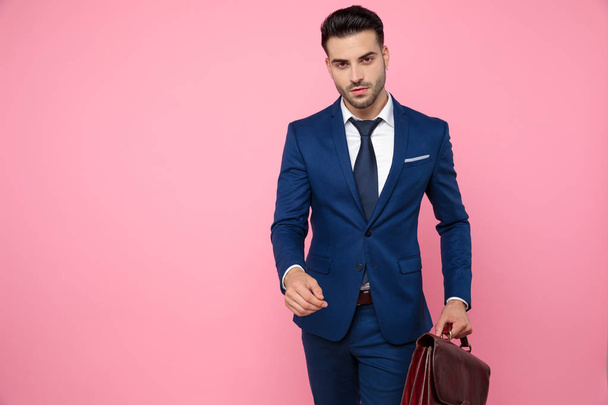 attraktive junge Mann mit Koffer und Fuß auf rosa Backgr - Foto, Bild