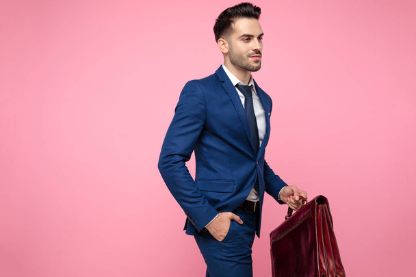 ελκυστικός νέος άντρας φορώντας μπλε κοστούμι και βαλίτσα - Φωτογραφία, εικόνα