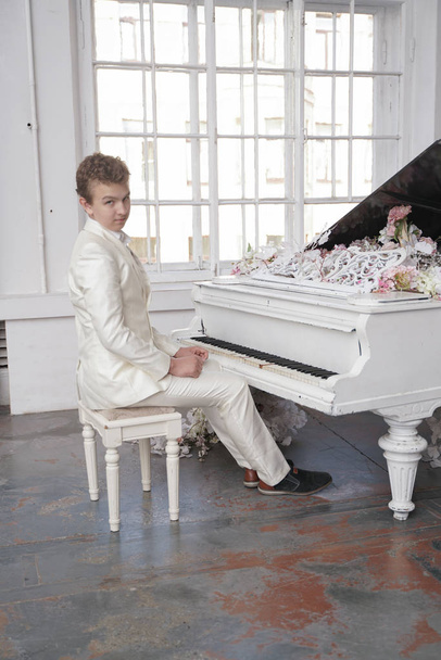 mladý muž dospívající v bílém obleku s velkým bílým klavírem v květech. Kavkazský samec hrají pouze na dovolené. - Fotografie, Obrázek