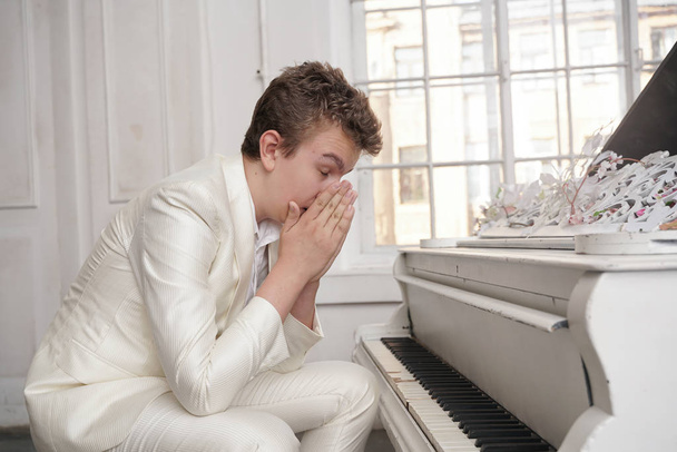 joven adolescente hombre en depresión con blanco gran piano de cola en el interior solo. chico odia la música y nervioso
 - Foto, Imagen
