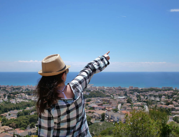 Attractive tourist in a hat shows a hand in front of him to the sky, standing on a hill - Foto, afbeelding