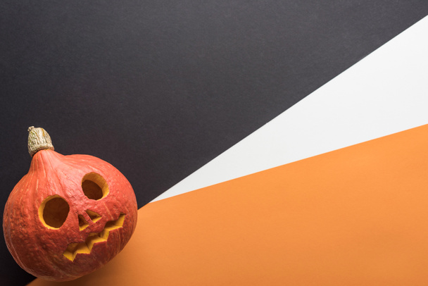 top view of spooky Halloween pumpkin on orange, white and black background - Фото, изображение