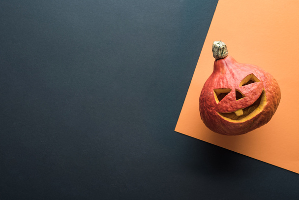 top view of spooky Halloween pumpkin on orange and black background - 写真・画像